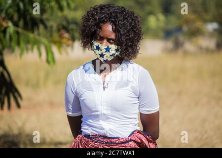 Frau trägt eine lokale handgemachte Gesichtsmaske aus traditionellem afrikanischen Stoff Sarong zum Schutz vor Corona-Virus Stockfoto