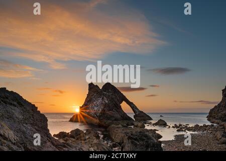 BOW FIDDLE ROCK PORTKNOCKIE MORAY COAST SCOTLAND SUMMER EIN MORGEN SONNENAUFGANG IM JULI EBBE BUNTE WOLKEN UND SONNENSTRAHLEN ÜBER DEM FELSEN Stockfoto