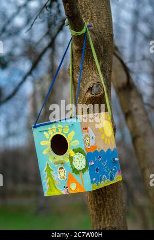 Vogelhaus, das an einem Baum in einem Stadtpark hängt. Lustige und bunte Farben schmücken seine Oberfläche. Stockfoto