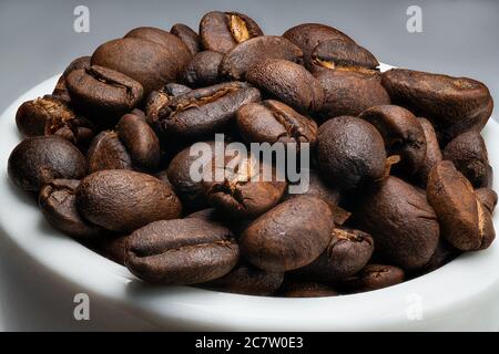 Extreme Nahaufnahme Makro eines Stapels gerösteter Kaffeebohnen in einer kleinen Tasse isoliert auf einem weißen und grauen Hintergrund Stockfoto