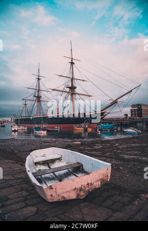 HMS Warrior vertäute in Portsmouth mit einem alten Fischerboot Im Vordergrund am Kai Stockfoto