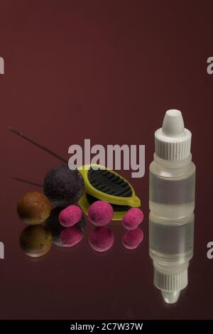 Nahaufnahme von karmesinroten Boilies, Flavour Flasche, Fischköder für Karpfen isoliert auf rotem Hintergrund. Stockfoto