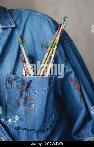 Nahaufnahme von Pinsel und Palettenmesser in der Tasche eines Jeanshemdes platziert. Stockfoto