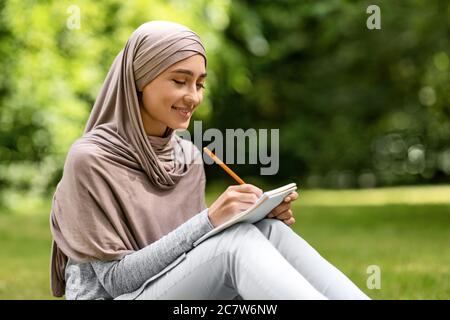 Mädchen in Hijab Schreiben auf Notebook, Studium im öffentlichen Park Stockfoto