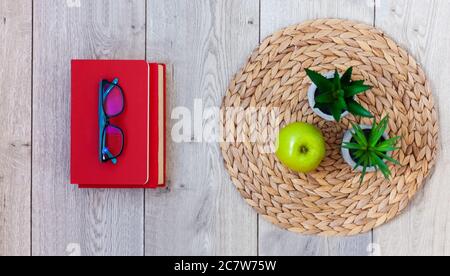 Zurück in die Schule, Stapel von Büchern in roten Abdeckungen, Gläser, grünen Apfel und Pflanzen in Töpfen auf einem Korbstand auf Holztisch. Fernunterricht. Quara Stockfoto