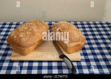 Zwei Laibe frisch gebackenes Brot mit Sesamsamen auf einem hölzernen Brotbrett Stockfoto