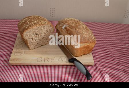 Zwei Laibe frisch gebackenes Brot mit Sesamsamen auf einem hölzernen Brotbrett Stockfoto