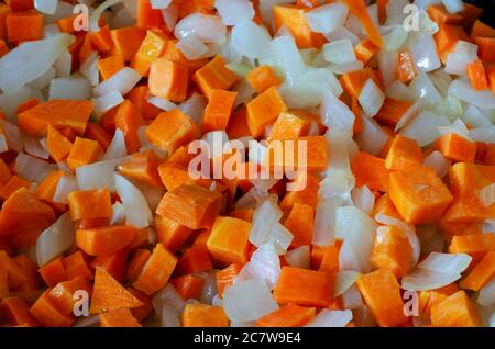 Gewürfelte weiße Zwiebeln und rohe Karotten Hintergrund. Scheiben roher Zwiebeln und Karotten aus der Nähe. Draufsicht in einem Winkel. Selektiver Fokus. Stockfoto