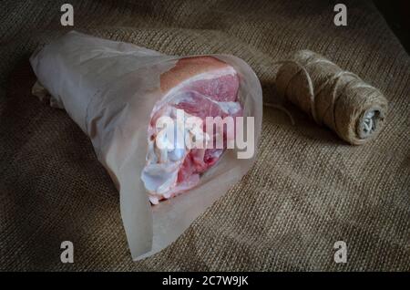 Rohes Schweineknöchel in Sackleinen-Geschenkpapier verpackt. Umweltfreundliche Verpackung von Produkten. Rohes Fleisch, Metzgerei. Seitenansicht. Selektiver Fokus. Stockfoto
