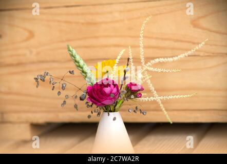 Mini Bouquet von wilden Blumen mit rosa Rose und gelben Mohn. Sommerliche Blumenkomposition. Wilde Blumen in Mini Vase isoliert auf Holzhintergrund Stockfoto