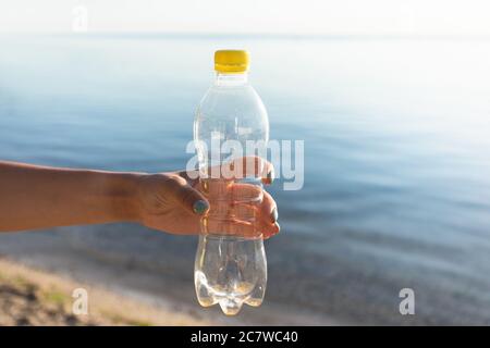 Weibliche Hand Halten Gebrauchte Plastikflasche Am Strand Im Freien, Abgeschnitten Stockfoto