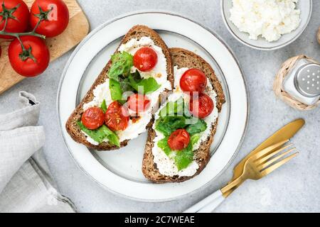 Bruschetta mit Ricotta-Käse, gerösteten Kirschtomaten und gehacktem Basilikum auf einem Teller. italienische Küche. Draufsicht Stockfoto