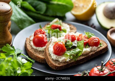 Leckeres Sandwich mit weichem weißen Ricotta-Käse, gerösteten Tomaten und Basilikum garniert mit zerkleinertem Pfeffer und Olivenöl Stockfoto