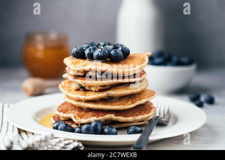 Haferpfannkuchen mit Heidelbeeren und Honig auf weißem Teller. Stapel von gesunden vegetarischen Pfannkuchen, Low Carb Paleo Pfannkuchen Stockfoto