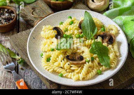 Gesunde Ernährung. Hausgemachte Pasta fusilli mit grünen Erbsen und gegrillten Champignons auf einem Holztisch. Stockfoto