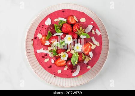 Roher veganer Beerenkake aus Cashew, Kirsche, Erdbeeren, Kokosnuss, Mandeln und Datteln mit frischen Beeren und Blumen. Köstliches Dessert. Top vie Stockfoto