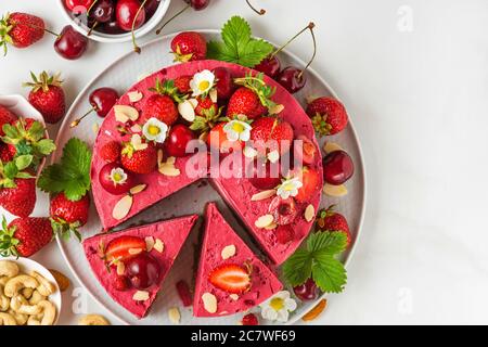 Roher veganer Brombeerenkochkuchen aus Cashew, Kirsche, Erdbeeren, Kokosnuss, Mandeln und Datteln mit frischen Beeren und Blumen. Köstliches Dessert. Stockfoto
