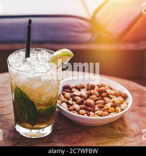 Mojito Cocktail. Erfrischendes Mojito Sommergetränk mit Stroh und Erdnüssen. Sonnenliege und Sonneneinstrahlung im Hintergrund. Bild Auf Lager. Stockfoto