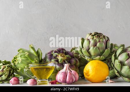 Gesundes veganes Lebensmittelkonzept. Frische reife Artischocken mit Olivenöl, Zitrone und Knoblauch auf Betongrund. Italienische Küche Küche Küche Hintergrund. Schließen U Stockfoto