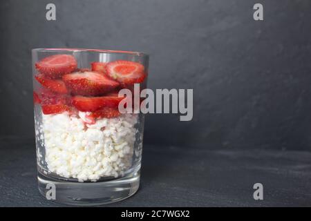 Frühstück in einer Glashütte Käse und Früchte Erdbeeren Beeren Schichten von gesunden Lebensmitteln steht auf einem grauen Stein schwarzen Hintergrund mit einem Platz zum Einfügen Stockfoto