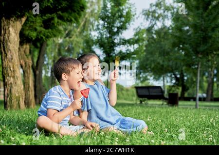 Zwei Kinder mit Lutschern sitzen im Sommer auf dem grünen Gras. Stockfoto