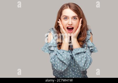 Oh mein gott, wow! Überrascht aufgeregt Brünette Mädchen Rüschen Bluse berühren Gesicht Blick auf Kamera erstaunt, offenen Mund in Erstaunen, schockiert von ungläubig Stockfoto