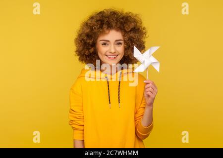 Origami Handmühle. Porträt von glücklich lockig-haarige Frau im urbanen Stil Hoodie lächelnd sorglos und halten Papier Windmühle, Windrad Spielzeug auf Stick. indo Stockfoto