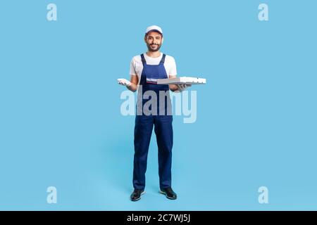 Volle Länge glücklich Kurier in Arbeitskleidung und Schutzhandschuhe tragen Pizza-Box, halten leeren Raum auf der Handfläche für Bild werben. Fast Food Delivery se Stockfoto