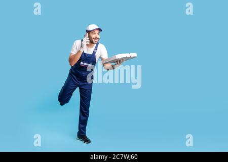 Express-Lieferservice. Voller Länge lustig glücklich Kurier Mann in Uniform sprechen am Telefon und läuft Pizza pünktlich zu geben, eilig zu liefern schnell Stockfoto