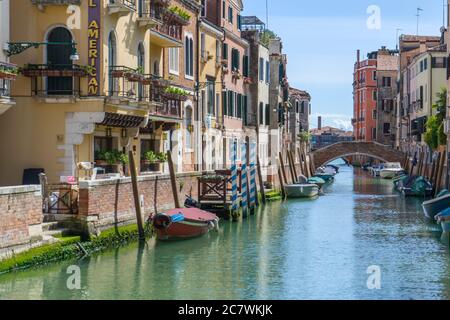 Schöner Blick auf einen Kanal in Venedig im Stadtteil Dorsoduro, an einem sonnigen Tag. Boote auf beiden Seiten des Kanals und eine Brücke im Hintergrund Stockfoto