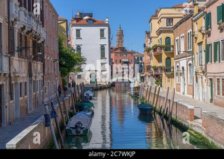 Schöner Blick auf einen Kanal in Venedig im Stadtteil Dorsoduro, an einem sonnigen Tag. Boote auf beiden Seiten des Kanals und eine Brücke im Hintergrund Stockfoto