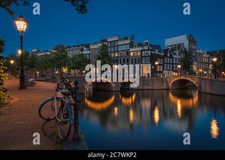 Das einsame Fahrrad neben den Kanälen bei Nacht im beleuchteten Amsterdam, Niederlande Stockfoto