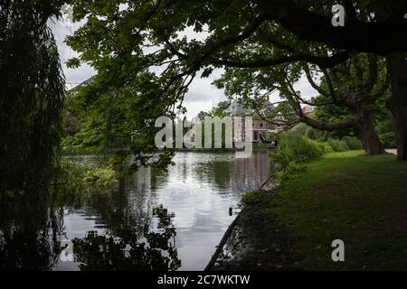 Unter den Bäumen ein Haus im Hintergrund in Vondelpark an einem bewölkten Tag, Amsterdam, Niederlande. Stockfoto