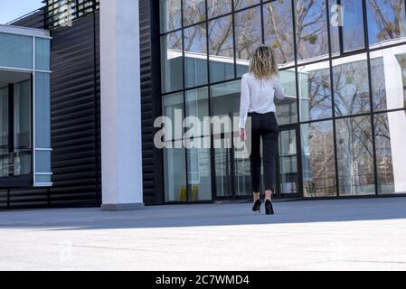 Junge kaukasische Geschäftsfrau, die vor dem Gebäude läuft und mit ihr spricht Mobiltelefon Stockfoto