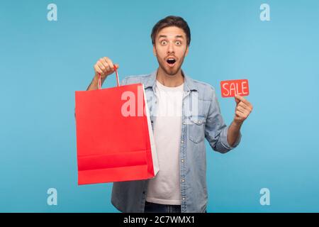 Portrait of Surrased Shopper man in Denim Shirt Holding Sale Inschrift und Pakete mit Platz für Werbung Text, Rabatt im Geschäft, Express Stockfoto