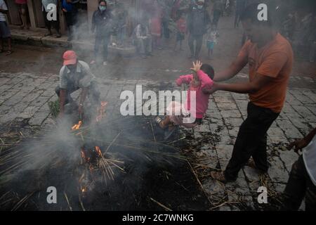 Ein Mann schwingt ein Kind um das Feuer, wo ein Bildnis des Dämons Ghantakarna verbrannt wurde, um die Zerstörung des Bösen zu symbolisieren und im Glauben böse Geister und Geister zu treiben, Während des Ghantakarna-Festivals, inmitten des Ausbruchs der Coronavirus-Krankheit (COVID-19), glaubten die Völker, dass das Fest böse Geister abwehrt und Frieden und Wohlstand in ihrem Leben bringt. In diesem Fest beten Menschen an und opfern Dämonen und übernatürlicher Macht Opfer. Stockfoto