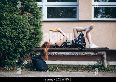 Teen, Ingwer Student Mädchen auf der Bank liegen, ein Buch lesen Stockfoto