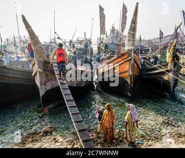 Chittagong, Bangladesch, 23. Dezember 2017: Fischer sind dabei, frischen Fang aus dem Boot zu entladen, während die einheimischen Frauen auf sie schauen Stockfoto