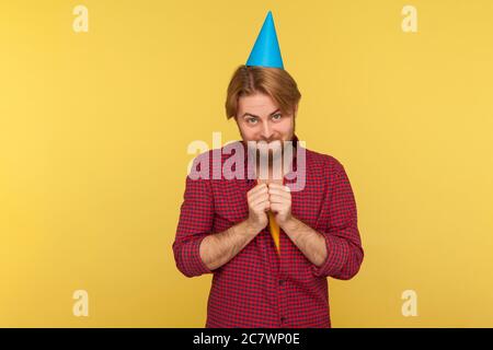 Fröhlicher Kerl mit lustigen Party-Kegel auf Kopf reiben Hände, lächelnd fröhlich gerissen als ob warten Geschenk, in Erwartung der Geburtstagsüberraschung. indoo Stockfoto