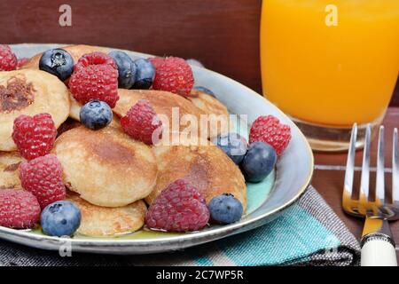 Mini-Pfannkuchen mit Beeren und Orangensaft auf Holztisch Stockfoto