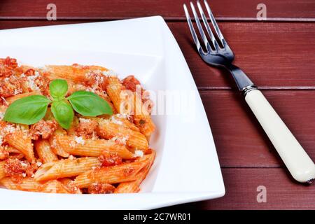 Penne mit Tomatensoße und Parmesan in einem Teller auf Holztisch Stockfoto