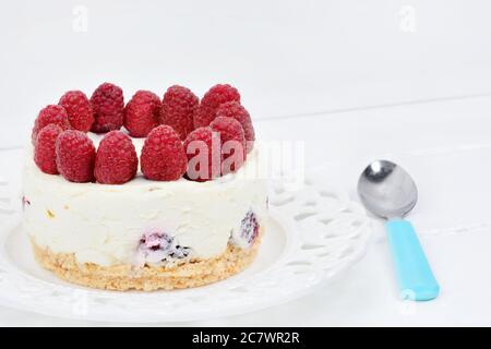 Mini-Käsekuchen mit weißer Schokolade und Himbeeren auf einem weißen Holztisch Stockfoto