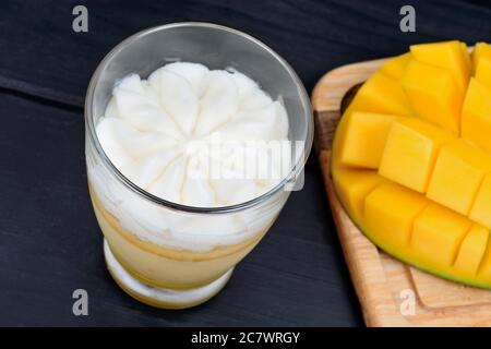 Nahaufnahme von Mousse von Mangofrucht mit Schlagsahne in einem Glas und Mangowürfel auf einem Tisch Stockfoto