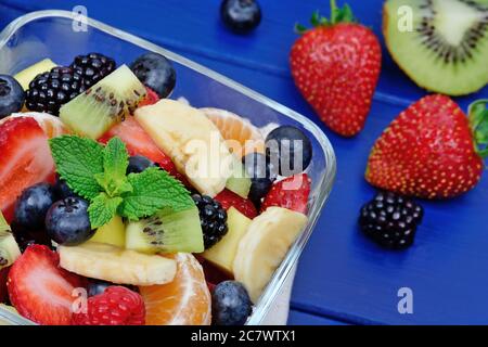 Nahaufnahme von Salat mit frischem Obst und Beeren in einer Schüssel auf blauem Holztisch. Draufsicht Stockfoto