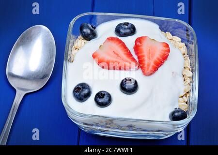 Hafer mit Joghurt und Früchten in einer Schüssel auf blauem Holztisch Stockfoto