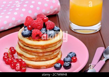 Leckere Pfannkuchen mit frischen Beeren in einem rosa Teller und Orangensaft auf dem Tisch Stockfoto