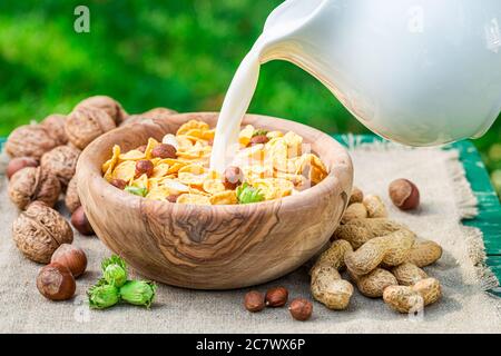 Milch in leckere Cornflakes mit Nüssen zum Frühstück gießen Stockfoto