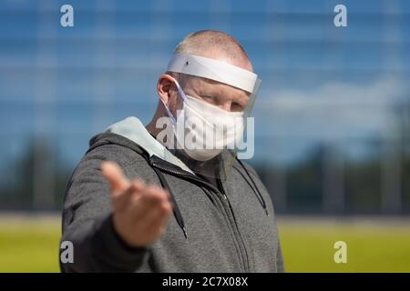 Erwachsene Mann posiert in einem schützenden transparenten Visier und einer weißen Maske auf seinem Gesicht im Freien an einem sonnigen Tag Stockfoto