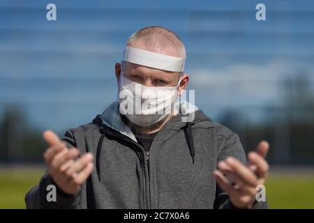 Erwachsene Mann posiert in einem schützenden transparenten Visier und einer weißen Maske auf seinem Gesicht im Freien an einem sonnigen Tag Stockfoto