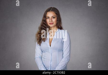 Porträt einer seriösen selbstbewussten Frau, die mit den Armen nach unten steht und auf Ihre Kamera schaut. Business Dame in blauem Hemd gewellt lange Haare. Isoliert auf grau-grauen s Stockfoto